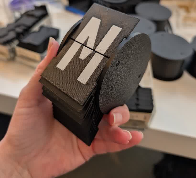 A single character module held in hand, showing the letters M and N incorrectly split across its two flaps.